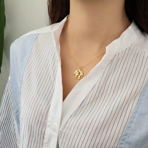 Detail of a minimalist gold-plated world map pendant necklace worn on the neck