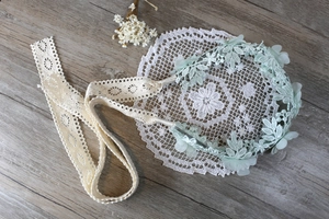 Diadema de encaje floral verde menta con bordados y cintas sobre fondo de madera vintage