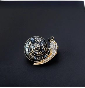 Detailed close-up of a snail brooch with black enamel, crystals, and gold filigree on leather