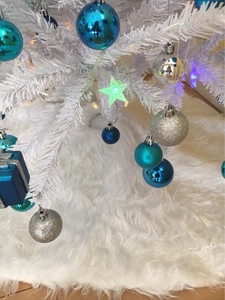 Detail of white faux fur Christmas tree skirt with blue and silver ornaments on a snowy tree