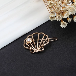 Golden shell-shaped metal hair clip with pearl accent on a minimalist dark background