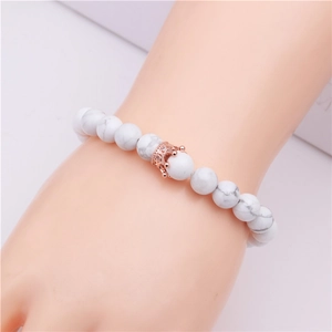 Vue détaillée d'un bracelet en perles de turquoise blanche avec couronne en or rose au poignet