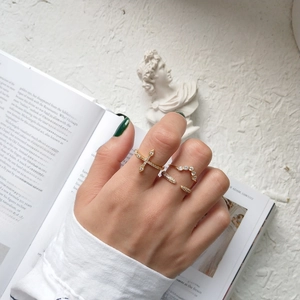 Detail of gold stackable cross ring and curved zircon band worn on finger over book