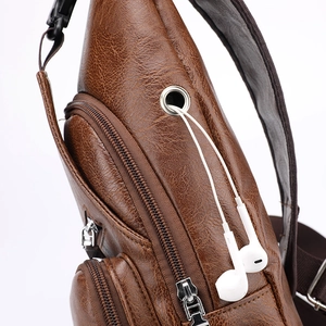 Detail of brown leather sling bag featuring a functional headphone port and zipper pockets