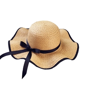 Summer wide brim straw sun hat with black ribbon bow and wavy edge for beach sun protection