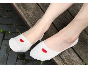 Gros plan de chaussettes basses beiges en coton avec broderie cœur rouge aux pieds