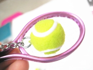 Close-up of a mini pink tennis racket and yellow ball keychain held in hand