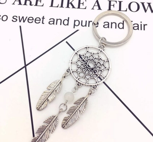 Detail view of silver dreamcatcher keychain with metallic feathers and a white bead charm