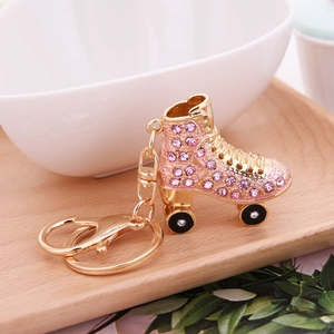 Pink rhinestone roller skate keychain with gold finish and black wheels on wooden tray
