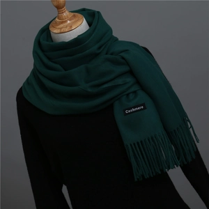 Detailed view of dark green cashmere scarf with fringe tassels on a black mannequin
