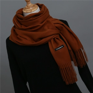 Detailed texture of caramel cashmere-like scarf with fringe and brand label on mannequin