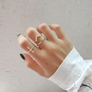 Close-up of a gold-tone minimalist cross ring and V-shaped pavé zircon ring set on hand