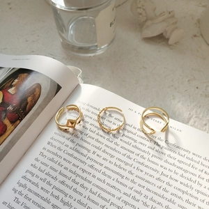 Three gold adjustable rings with geometric layered designs on a vintage art book background