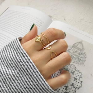Set of minimalist geometric gold rings shown worn on hand over a vintage book page