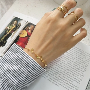 Detail of gold disc charm bracelet and geometric rings styled on a model's hand
