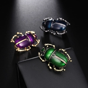 Trio de broches scarabée vintage en émail vert, violet et bleu sur un fond noir profond