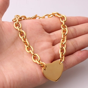 Close-up of a hand holding a polished gold stainless steel chain bracelet with heart charm