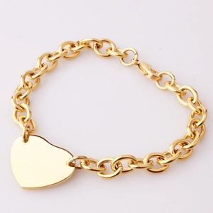 Detail shot of golden chunky chain link bracelet with a heart charm on white backdrop