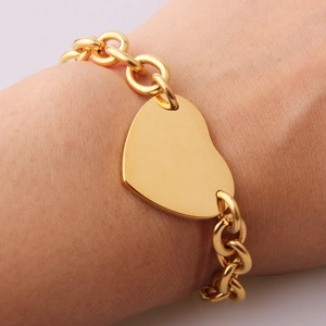 Detailed view of a gold heart pendant bracelet worn on wrist with oval link chain