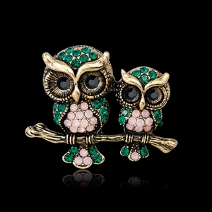 Vintage owl brooch with green and pink rhinestones on gold branch, front view on black background