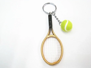 Detail view of miniature gold tennis racket and green ball keychain on white background