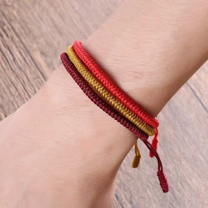 Detail of three handmade braided knot bracelets in red, gold and burgundy on wrist