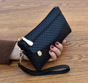 Close-up of black quilted clutch bag featuring a gold zipper and a wrist strap