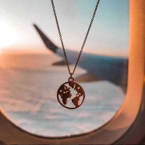Gold-plated 925 sterling silver world map pendant necklace against a sunset airplane window