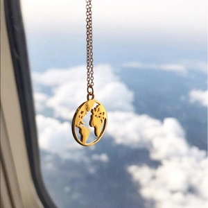 Detailed view of a gold world map pendant necklace styled against a blue sky background