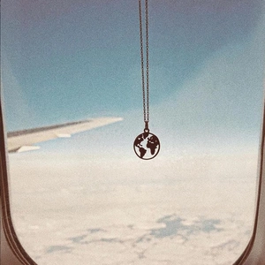Detailed view of gold world map necklace against airplane window and clouds background