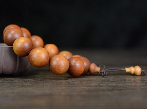 Close-up of polished sandalwood prayer beads draped on a dark ceramic vessel