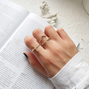 Detailed view of layered gold cross ring and shimmering pave zircon bands on a finger