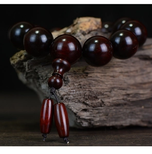 Close-up of polished Red Sandalwood beads with natural wood grain on a rustic wood branch