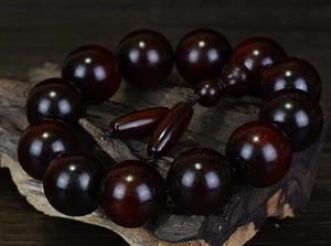 Detailed close-up of dark red sandalwood beads displayed on a natural wood branch