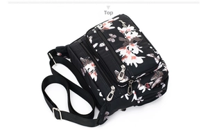 Top view of black floral nylon bag showing multiple metal zippers and layered pockets