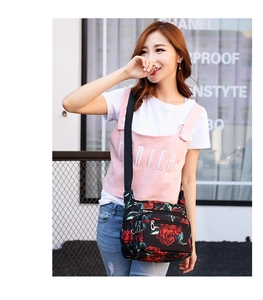 Outdoor model wearing a black floral nylon crossbody bag with red rose prints and multiple pockets