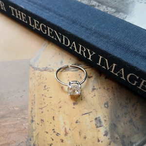 Macro shot of S925 silver ring featuring a princess-cut zircon next to a blue book