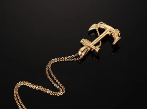 Macro view of golden anchor pendant with rope detail on a reflective black background