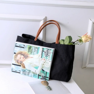 Detail of a large black canvas tote bag with brown leather handles on a bright table