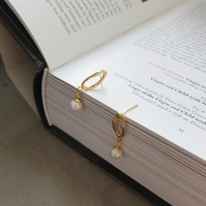 Detail view of gold irregular oval earrings with white pearls on artistic book background