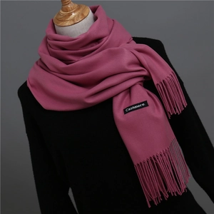 Detail of soft cashmere feel scarf in deep pink featuring fringe and brand label