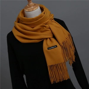Detailed close-up of mustard yellow cashmere scarf with fringe and authentic woven label