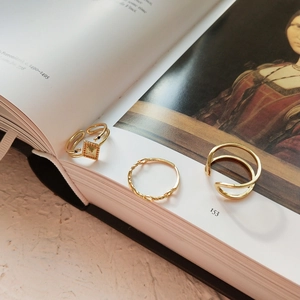 Detailed view of three gold geometric rings layered on an artistic open book page