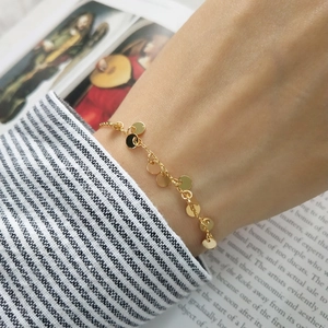 Close-up of a delicate gold chain bracelet with round charms worn on a wrist