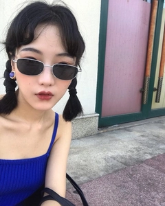 Detalle de gafas de sol cuadradas de metal con lentes gris humo usadas en exterior por modelo