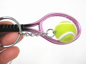 Close-up of a mini pink tennis racket and yellow fuzzy ball keychain held in hand