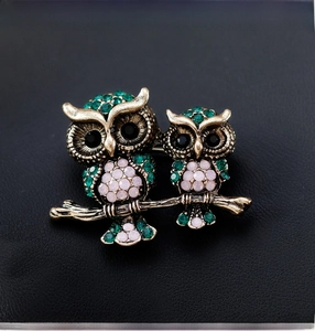 Macro shot of vintage owl brooch with green and pink crystals on dark leather