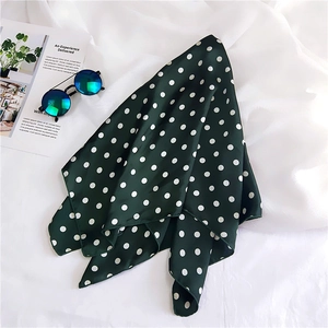 Close-up of dark green polka dot silk scarf with sunglasses on a white textured background