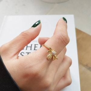Detail of a golden bee ring with pavé zircons worn on a finger over a book background