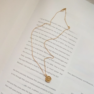 Detail of a vintage gold coin necklace with fleur-de-lis relief on open book pages